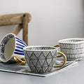Tasse mit abstraktem geometrischem Muster und Goldhenkel